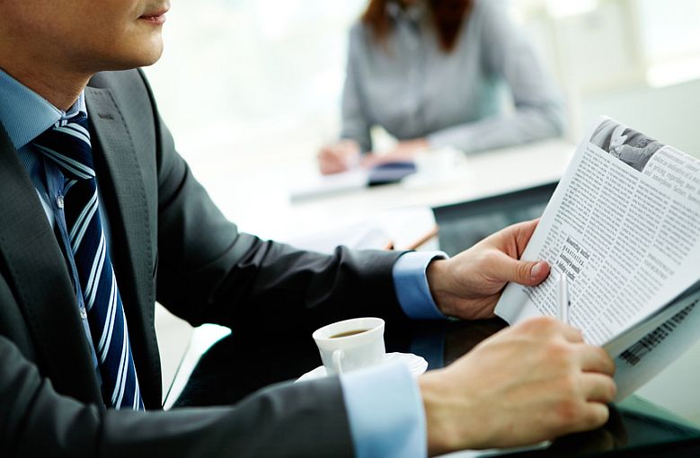 Image of male in suit with newspaper reading it in office