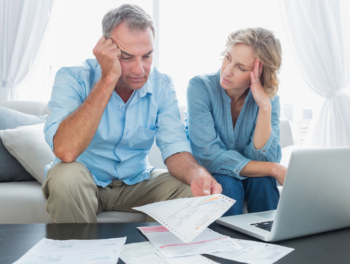 Worried couple using their laptop to pay their bills at home in the living room